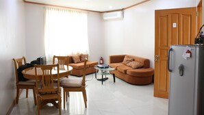 A living room with a dining table, chairs, a sofa, a glass coffee table, and a refrigerator. - Dumaguete Springs Apartment (Dumaguete)