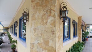 A building with a stone facade, multiple windows with blue frames, and outdoor lighting fixtures. - Dumaguete Springs Apartment (Dumaguete)
