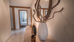 A hallway with a large vase and decorative branches on a table, leading to a bedroom with a bed and curtains. - Löwenplatz Apartment near Station by Airhome (Zürich)