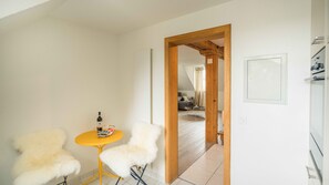A room with a yellow table and two white chairs, a bottle on the table, and a wooden door leading to another room.