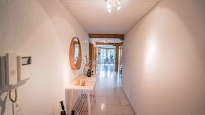 A hallway with a white tiled floor, a wooden door frame, a small table with a vase and candles, and a wall-mounted mirror. - Löwenplatz Apartment near Station by Airhome (Zürich)