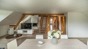Un salon moderne avec un escalier en bois, un téléviseur à écran plat et un coin repas agrémenté d’un vase de fleurs.