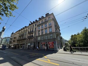 A multi-story building with a classic architectural style, featuring a ground-level entrance with a red awning and a visible sign. - Löwenplatz Apartment near Station by Airhome (Zürich)