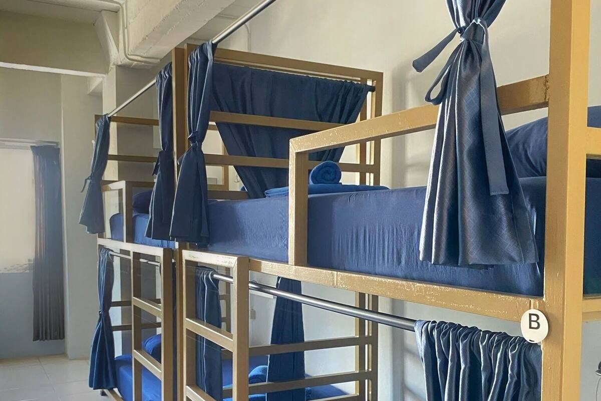 Une chambre de dortoir avec des lits superposés, chacun étant muni d’un rideau fixé au niveau de la tête de lit.