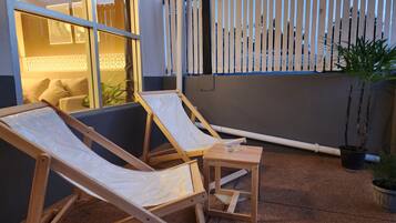 Two wooden lounge chairs with white cushions, a small wooden table, and a potted plant.