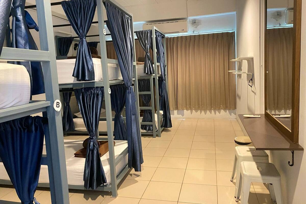 Une chambre de dortoir avec des lits superposés, un bureau, un miroir et une fenêtre avec des rideaux.