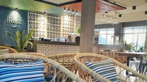 Un área de estar con sillones de mimbre y cojines a rayas, un mostrador de recepción y una pared con diseño geométrico.