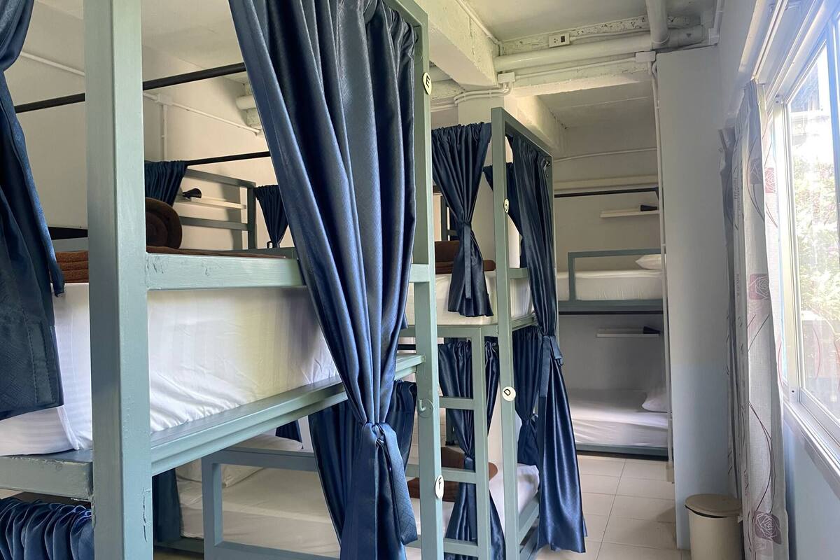 Une chambre de dortoir avec des lits superposés, chacun étant muni d’un rideau. On peut voir une échelle sur l’un des lits superposés, ainsi qu’une poubelle.