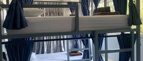 Dormitorio con literas, cortinas azules, ropa de cama blanca y una mesa de madera.