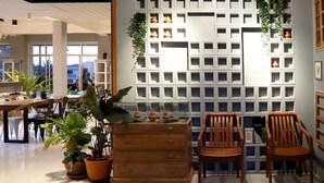 Una zona de recepción con un escritorio de madera, dos sillas de madera, una planta en maceta y una pared con varios estantes cuadrados.