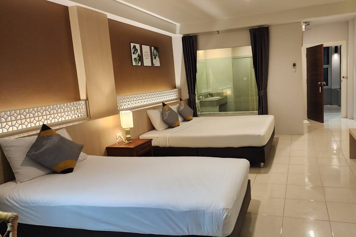 Une chambre d’hôtel avec deux lits, un bureau, une salle de bain visible à travers une paroi en verre et un téléviseur posé sur le bureau.