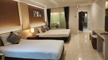 A hotel room with two beds, a desk, a bathroom visible through a glass partition, and a TV on the desk.