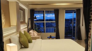 Habitación de hotel con una cama grande, una mesita de noche, una lámpara y vistas a la ciudad a través de las ventanas.