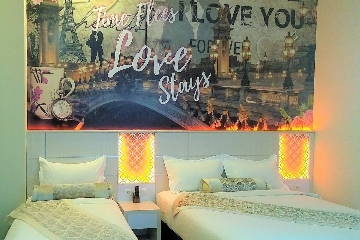 A hotel room with two beds, a decorative wall with a romantic theme, and a view of a bridge.
