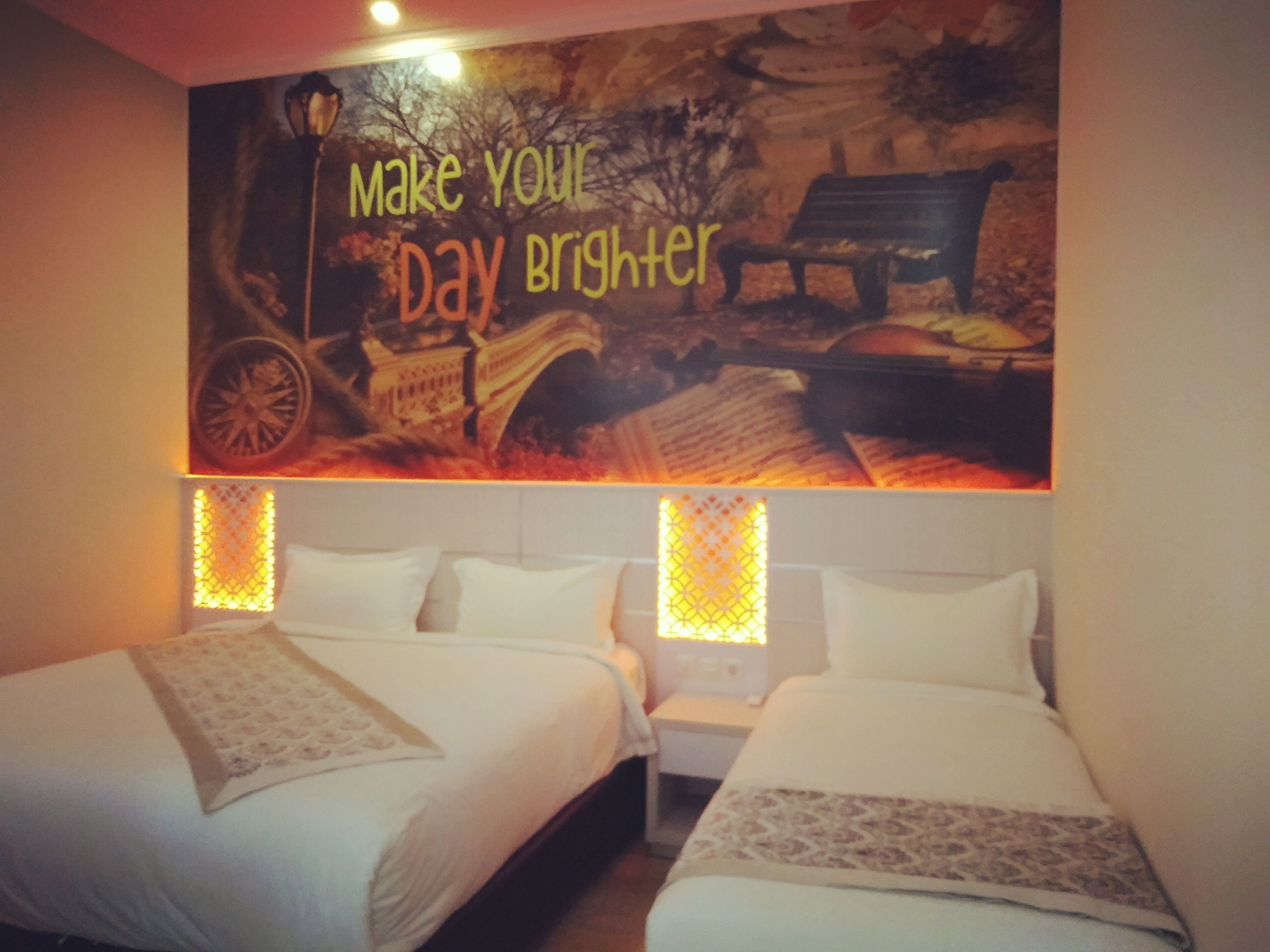 Una habitación de hotel con dos camas, un mural en la pared y un banco.