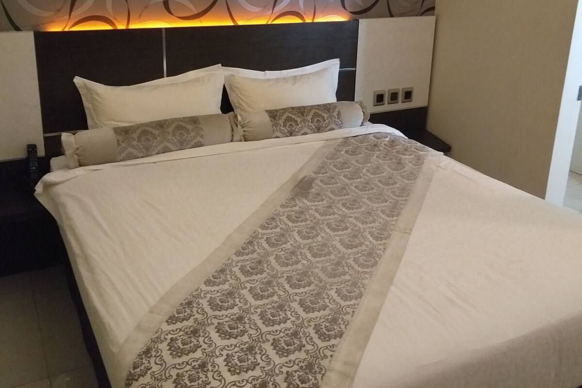 A neatly made bed with a patterned bedspread, a headboard with a circular design, and a wall with a similar pattern.