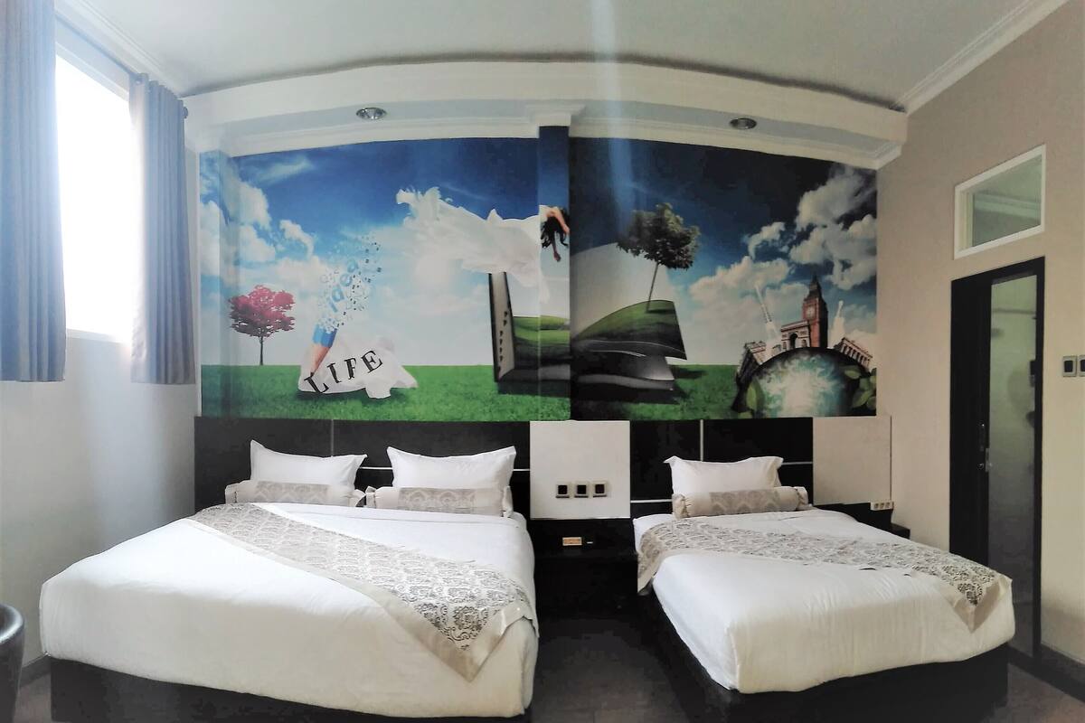 A hotel room with two beds, a large mural on the wall, and a window with curtains.