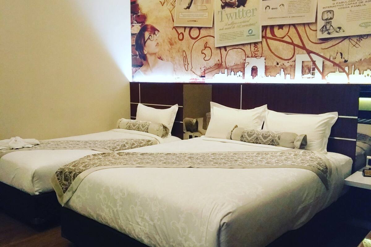 A hotel room with two beds, a large wall mural with social media logos, and a wooden floor.