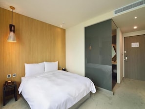 A modern hotel room with a large bed, a wooden accent wall, a glass partition, and a door leading to a bathroom.