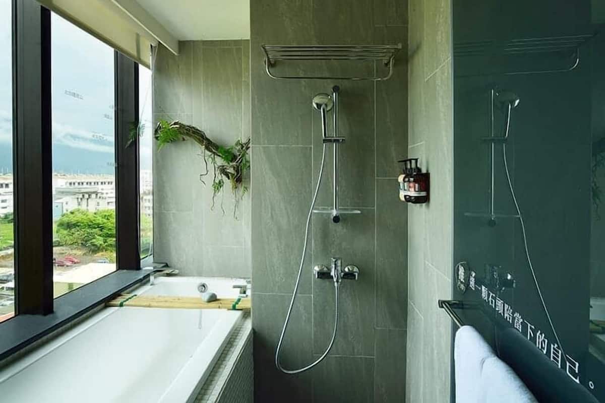 A modern bathroom with a bathtub, a shower with a rain showerhead, and a large window offering a city view.