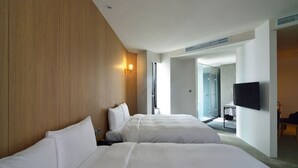 Habitación de hotel con dos camas, cabecero de madera, televisor montado en la pared y puerta del baño visible.