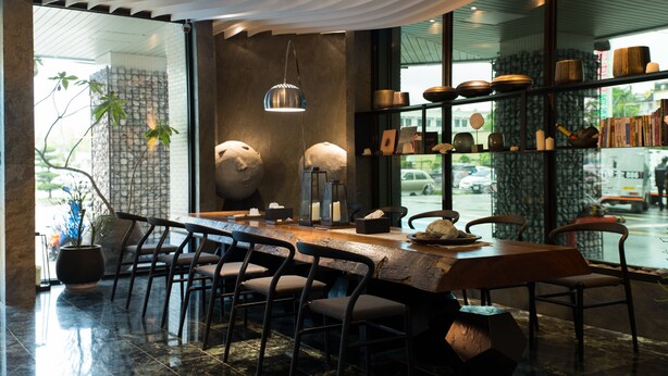 Zona de bar moderna con una barra larga, varios taburetes y una planta grande en maceta.