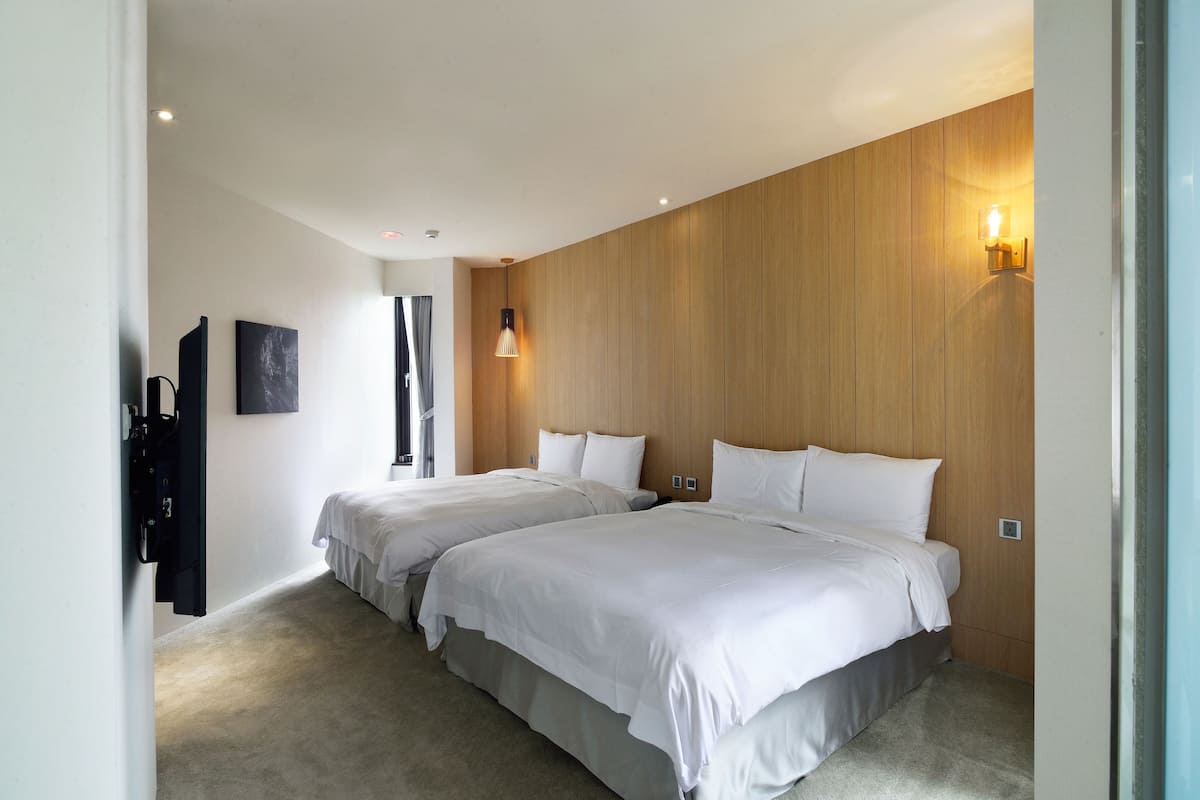 A modern hotel room with two beds, a wooden accent wall, and a light fixture.