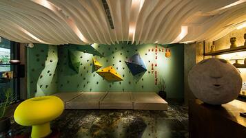 A modern interior with a green wall featuring climbing holds, a yellow and a beige chair, and a large stone sculpture.