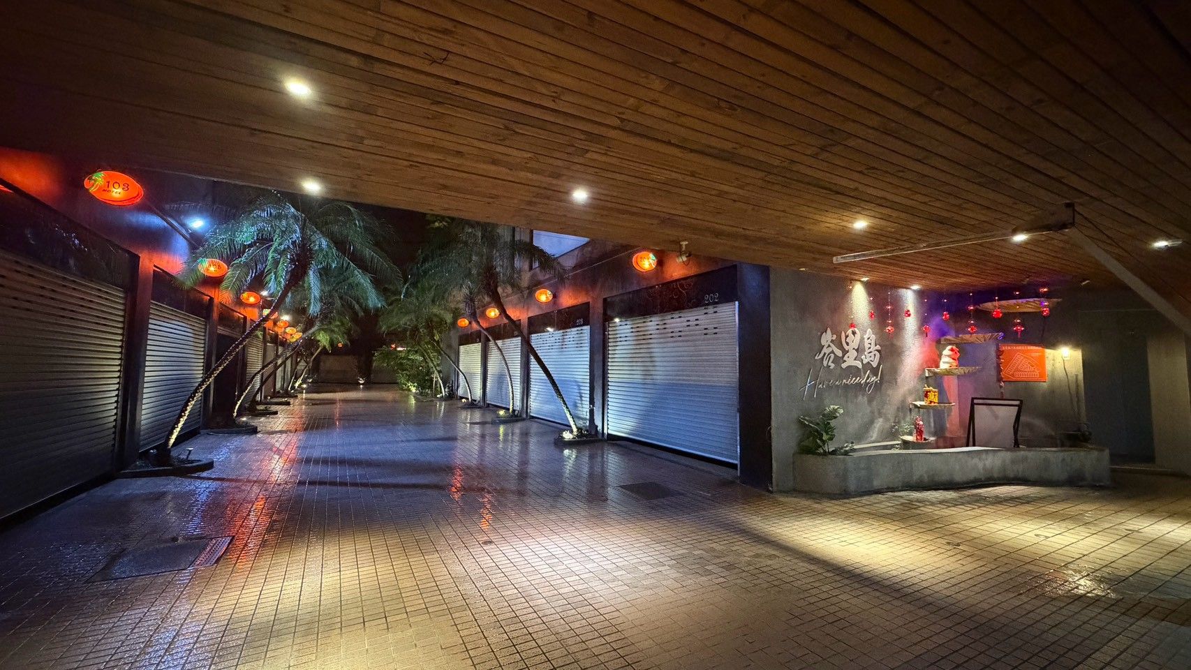 Un espacio al aire libre techado, con suelo de baldosas, palmeras y un escenario decorado.