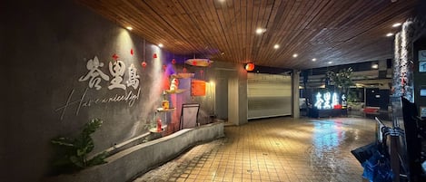 Zona de recepción de un hotel con suelo de baldosas, un mostrador de recepción y una pared con detalles decorativos.