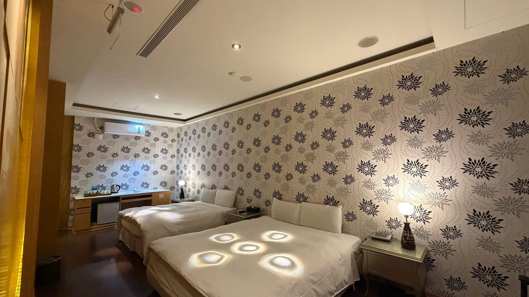 A hotel room with two beds, a desk, and a small kitchenette.