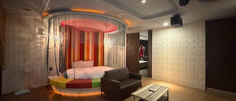 Un dormitorio moderno con cama, sofá, mesa de centro y un original ventanal circular.