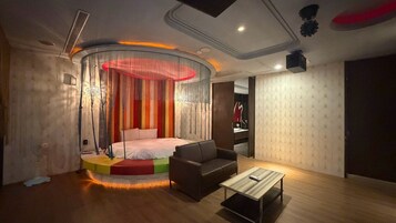 Un dormitorio moderno con cama, sofá, mesa de centro y un original ventanal circular.