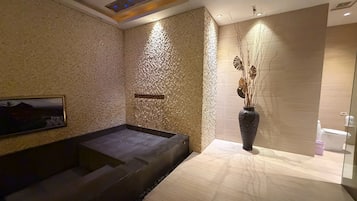 A spa area with a hot tub, a wall-mounted massage table, and a large vase with dried plants.