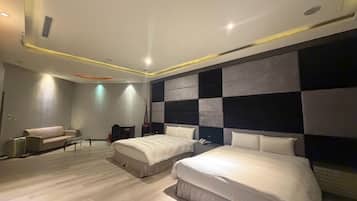 Quarto de hotel moderno com duas camas, um sofá, uma mesa pequena e um painel decorativo na parede.