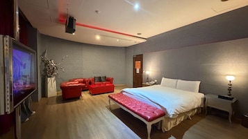 Una habitación de hotel moderna con una cama grande, un sofá rojo, un televisor de pantalla plana y una mesita de noche con lámpara.
