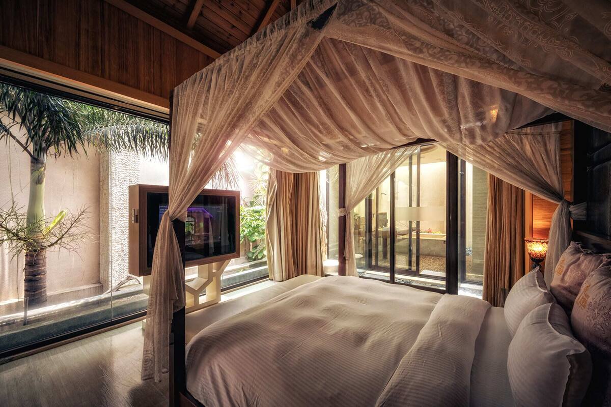 Une chambre à coucher avec un lit à baldaquin, de grandes fenêtres et une vue sur l’extérieur.
