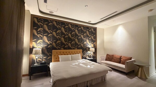 A hotel room with a large bed, a sofa, a nightstand with lamps, and a patterned wallpaper.