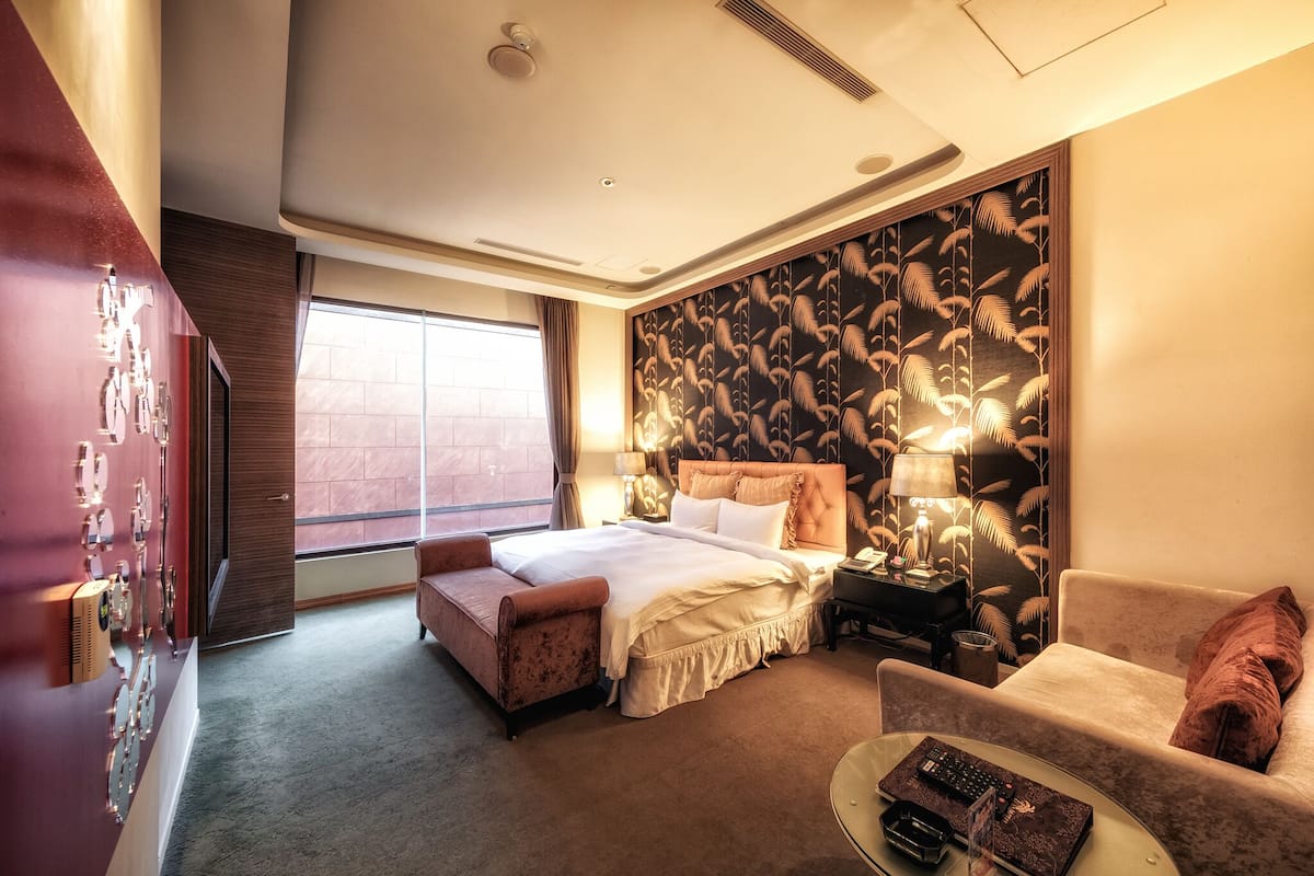 Une chambre d’hôtel dotée d’un grand lit, d’un coin salon avec un canapé et un fauteuil, d’une petite table et d’un panneau décoratif mural.