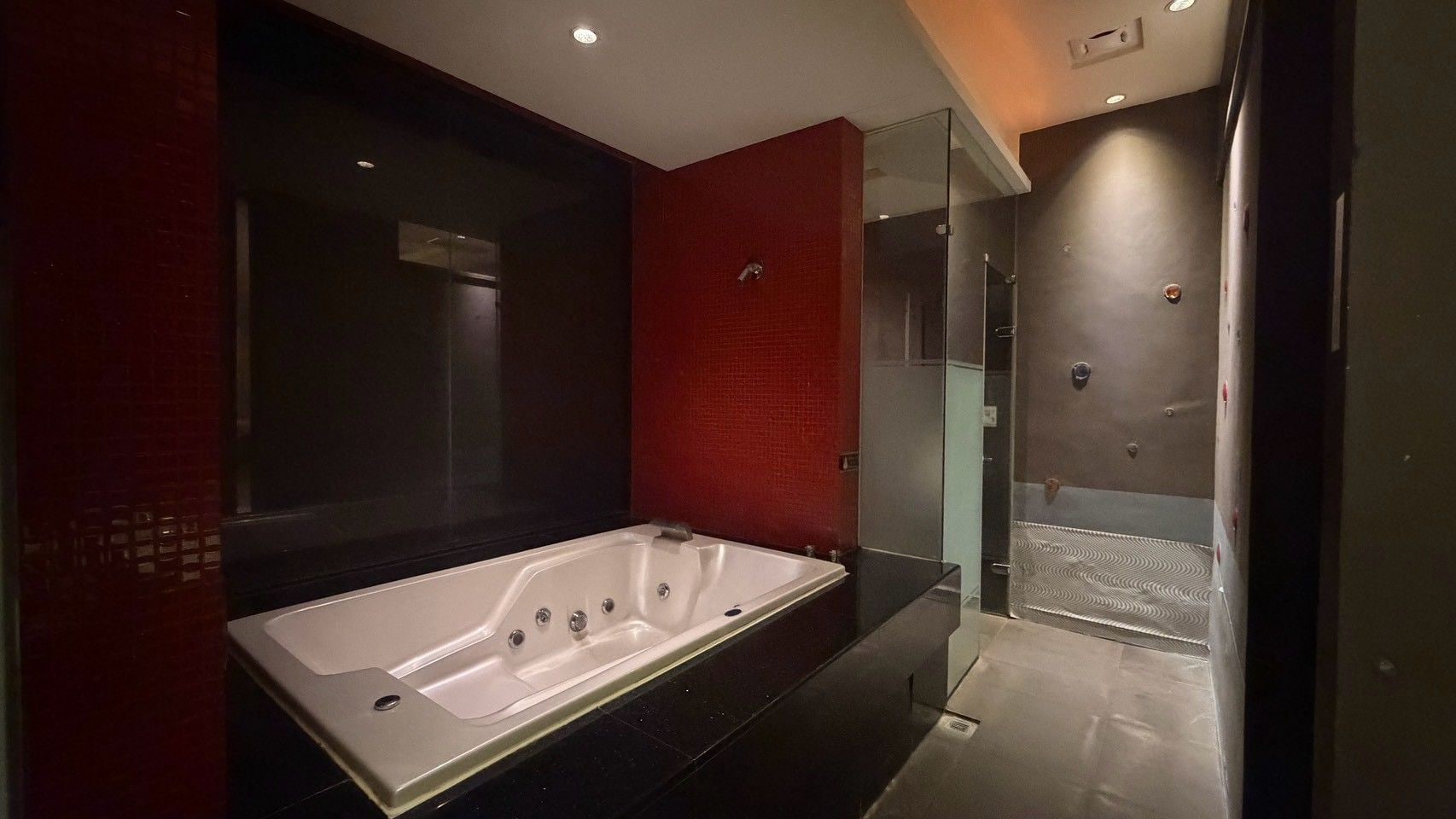 A modern bathroom with a large bathtub, a glass shower enclosure, and a red accent wall.