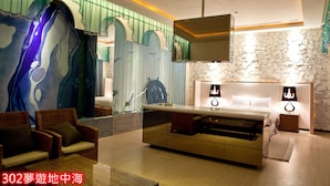 Quarto de hotel moderno com uma cama grande, um sofá, uma televisão e uma parede decorativa com design de cascata.