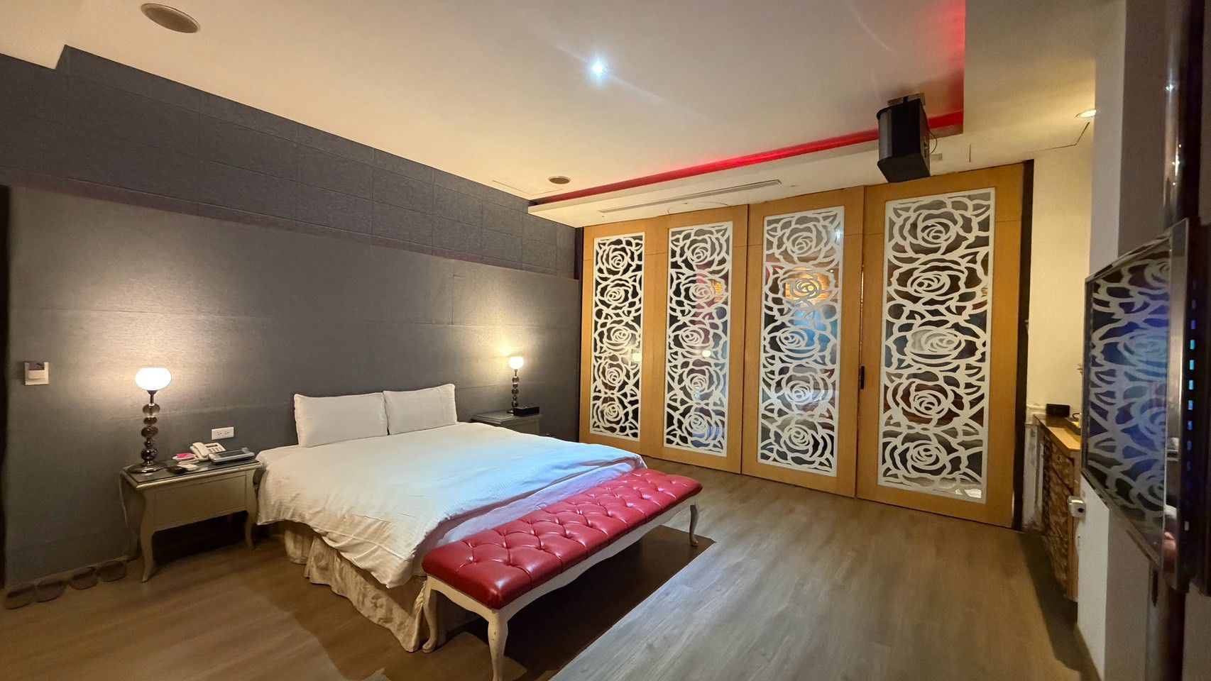 Une chambre d’hôtel comprenant un lit, des tables de chevet, un banc et des panneaux décoratifs.