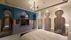 Een hotelkamer met een groot bed, een aan de muur bevestigde televisie, een kroonluchter en een spiegel met verticale strepen.