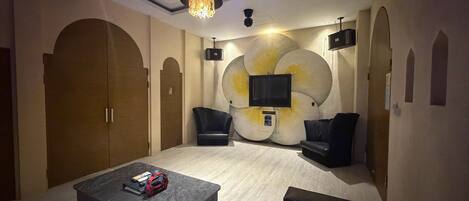 A room with a bed, two armchairs, a coffee table, a TV, and a chandelier.