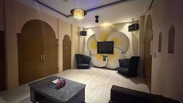A room with a bed, two armchairs, a coffee table, a TV, and a chandelier.