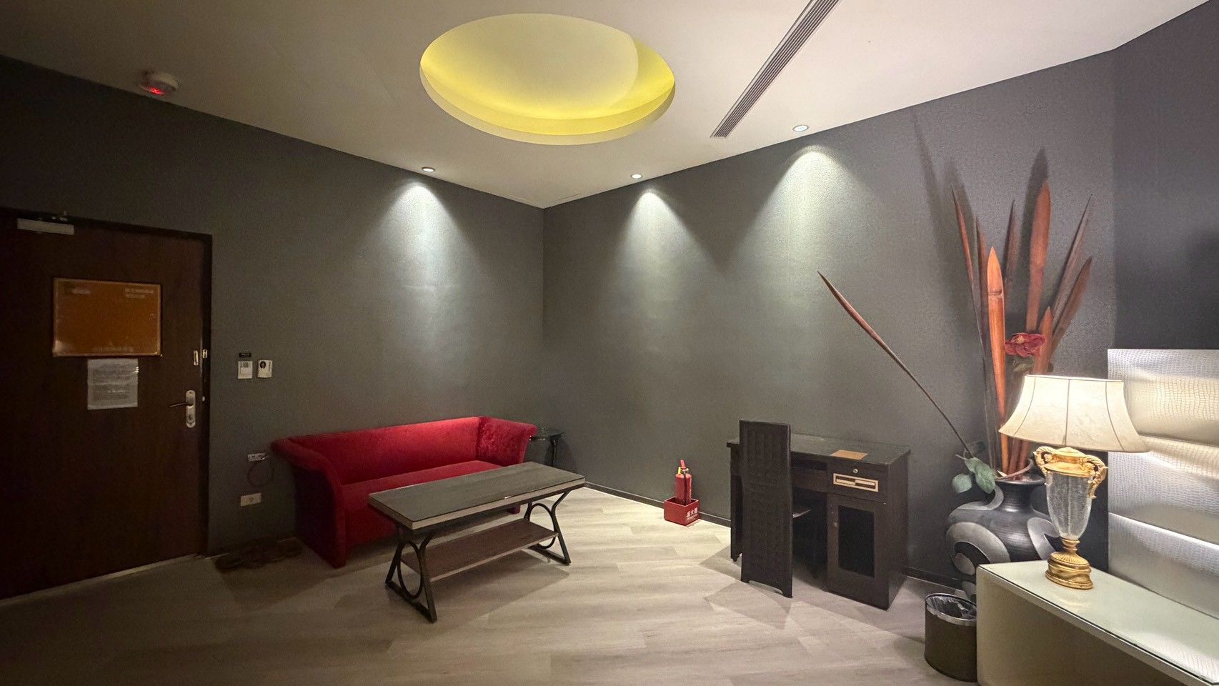 Una habitación con un sofá rojo, una mesita, una lámpara y un jarrón decorativo.