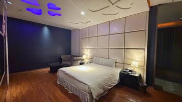 A modern bedroom with a large bed, a nightstand with a lamp, and a dark-colored wall.