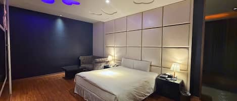 Un dormitorio moderno con una cama grande, una mesita de noche con lámpara y una pared de color oscuro.