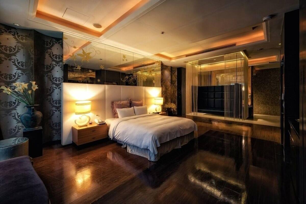 Une chambre à coucher moderne avec un grand lit, des lampes de chevet, une table de nuit, un miroir et une fenêtre avec des stores.