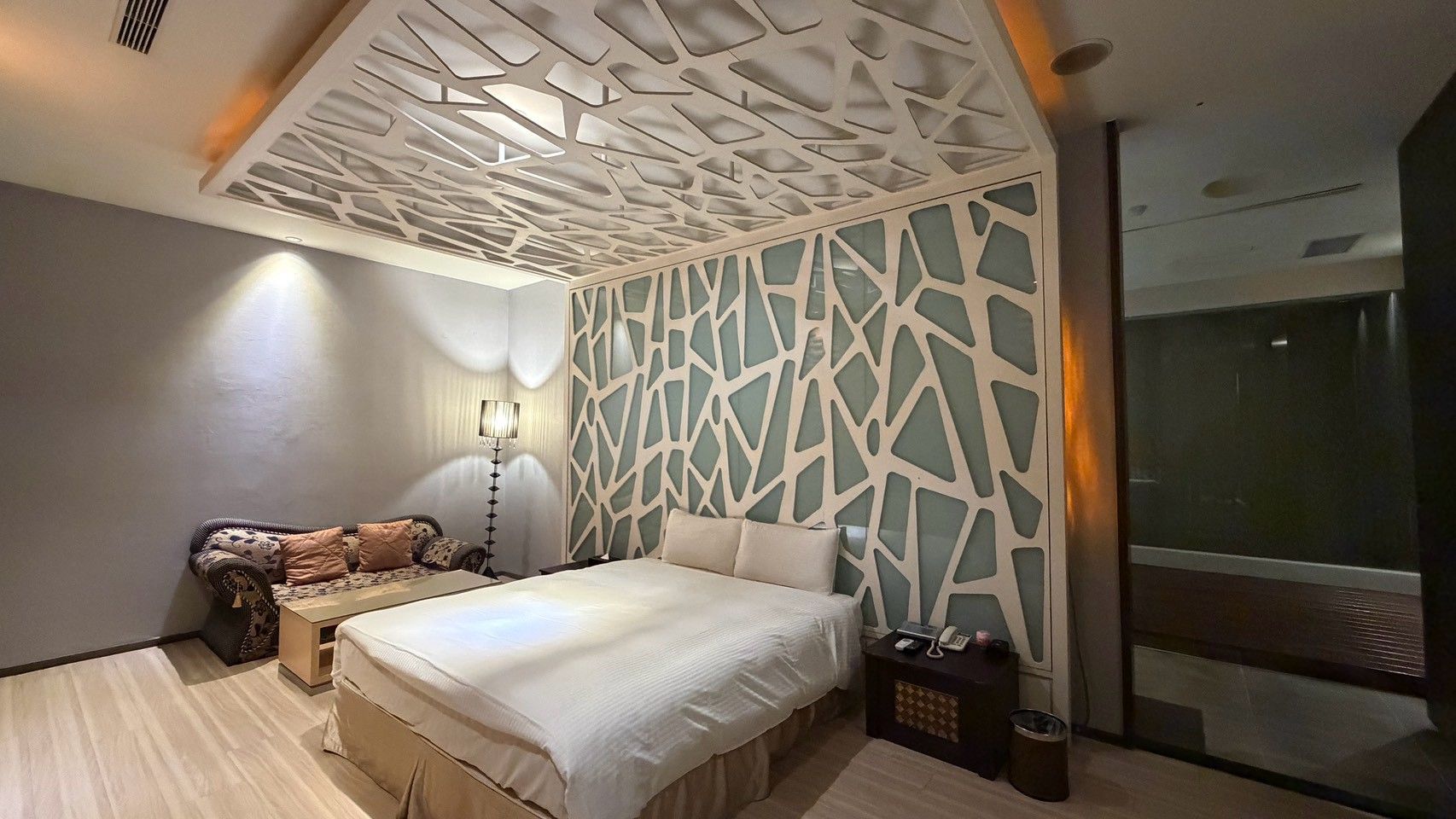A modern bedroom with a bed, a sofa, a nightstand, and a decorative wall panel.